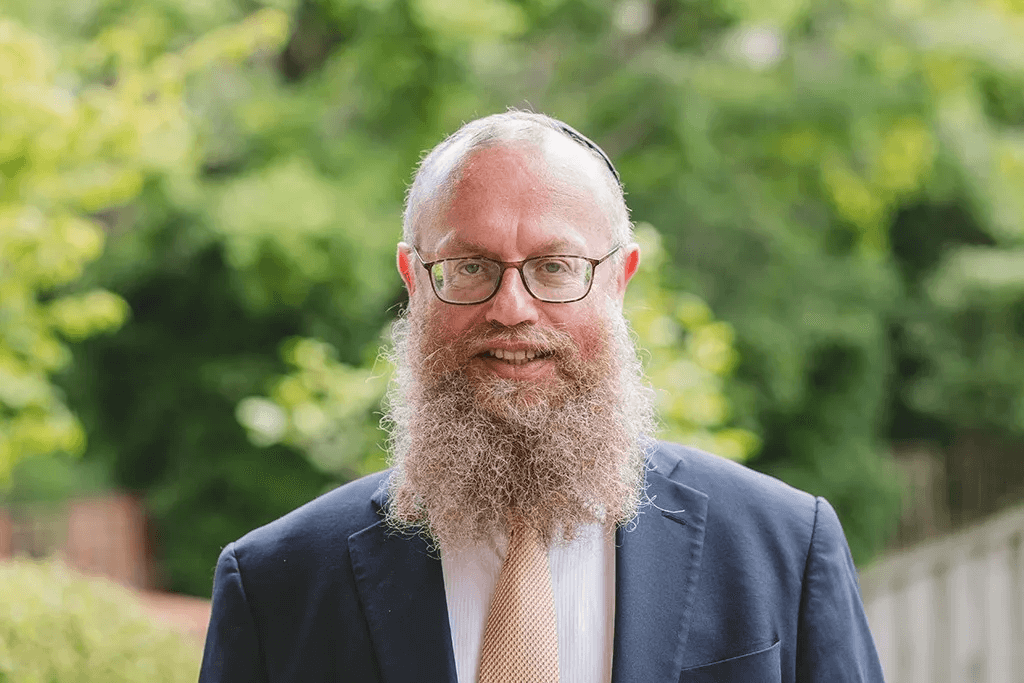 A man with long beard and glasses in suit.